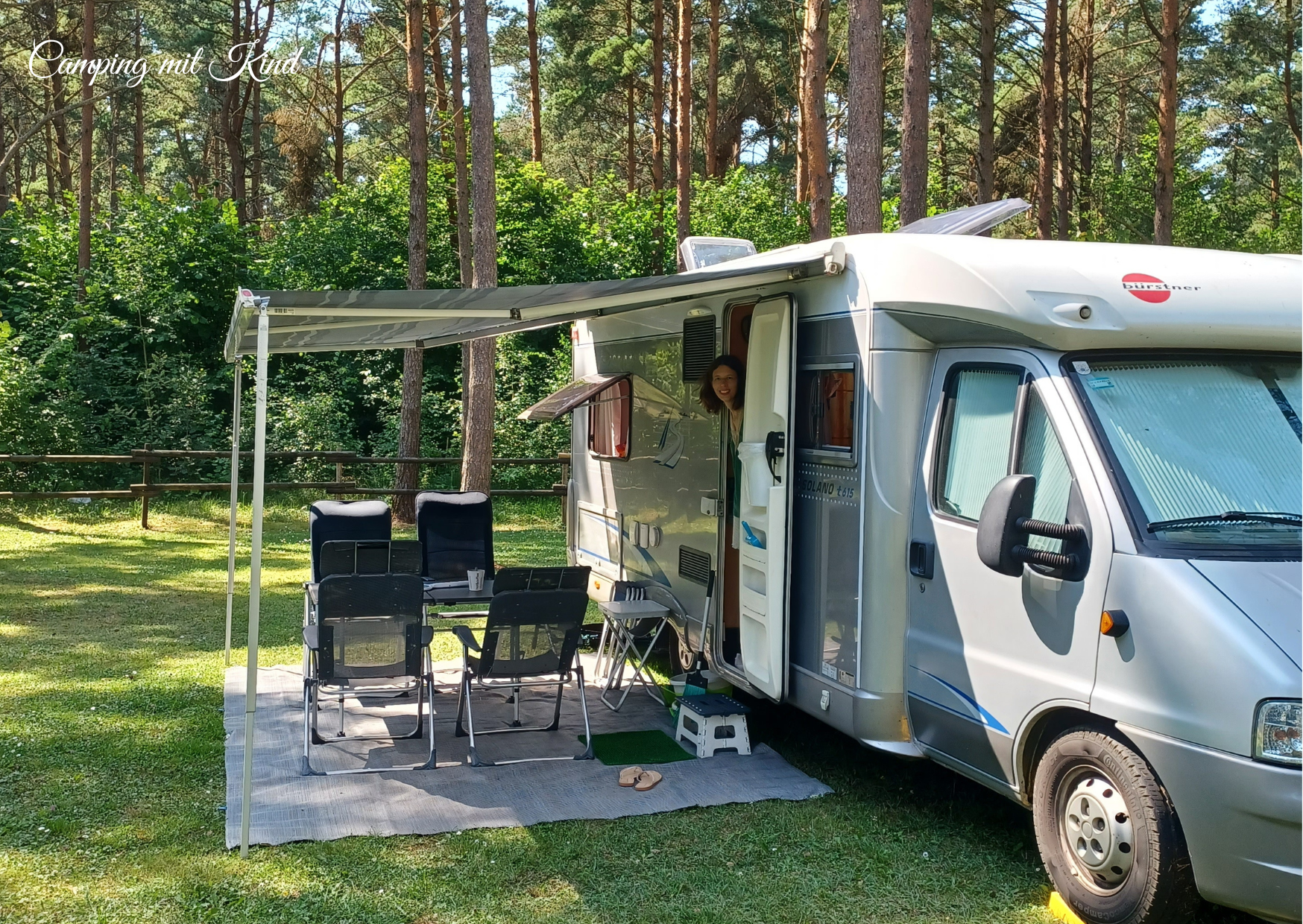 Ein Wohnmobil steht auf einer Wiese. Die Markise ist herausgefahren, darunter stehen Campingstühle und ein Campingtisch.