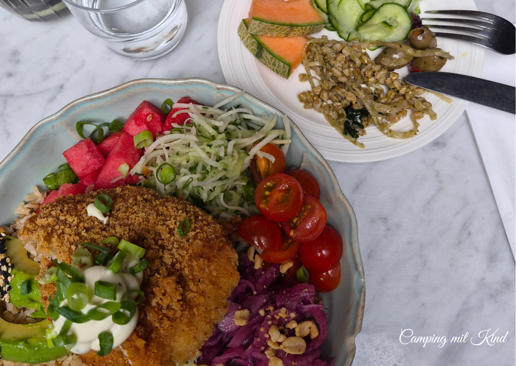 Auf dem Tisch befindet sich ein Teller mit Wassermelonenstücken, paniertes Fleisch, Salat und ein Glas Wasser