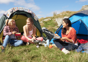 3 Mädchen sitzen vor einem Zelt.
