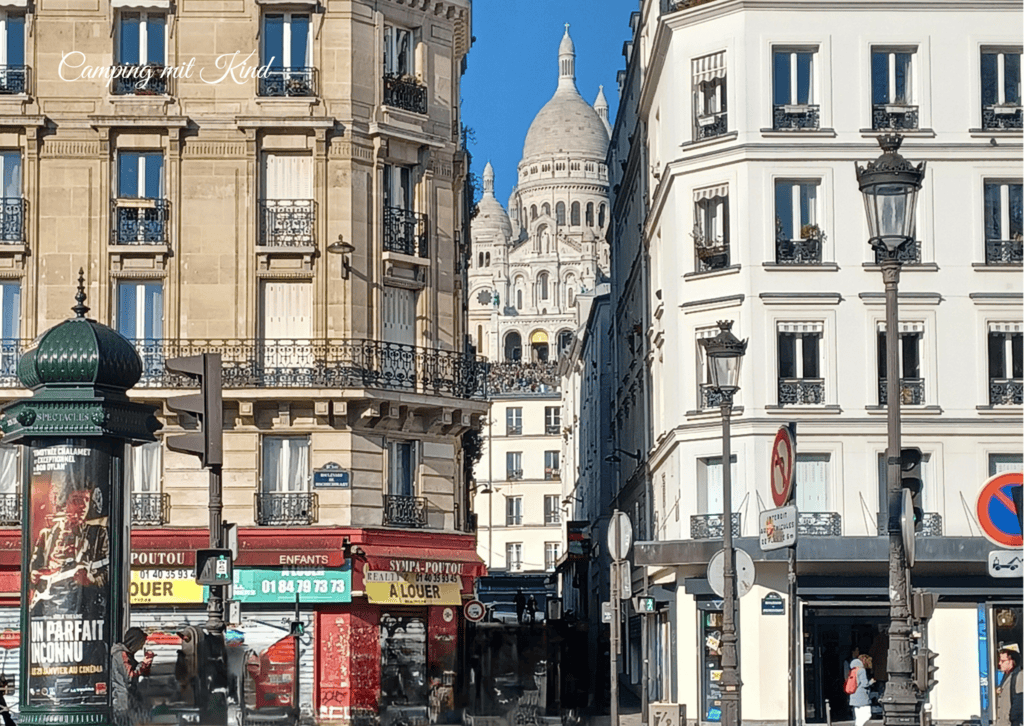 Links und rechts befinden sich hohe Häuser, dazwischen befindet sich die Basilika Sacre Coeur