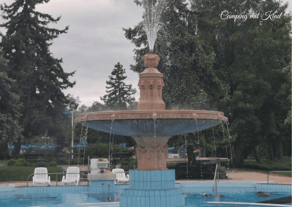 Ein Springbrunnen , dahinter stehen Bäume.