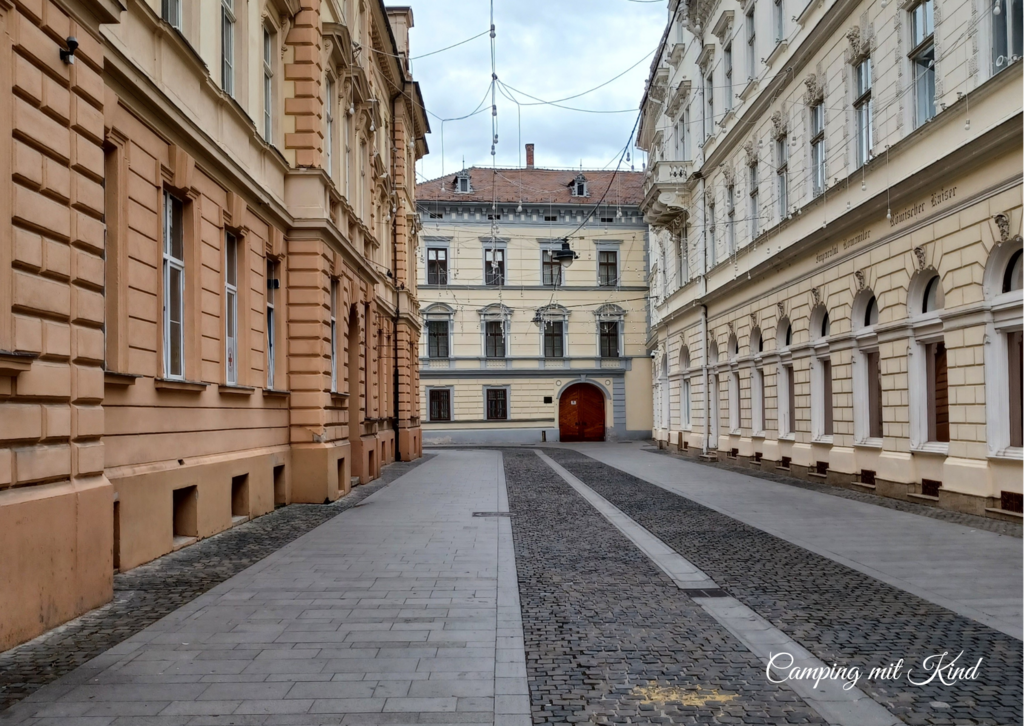Links und rechts befinden sich Häuserfronten. In der Mitte eine Gasse mit Pflastersteinen