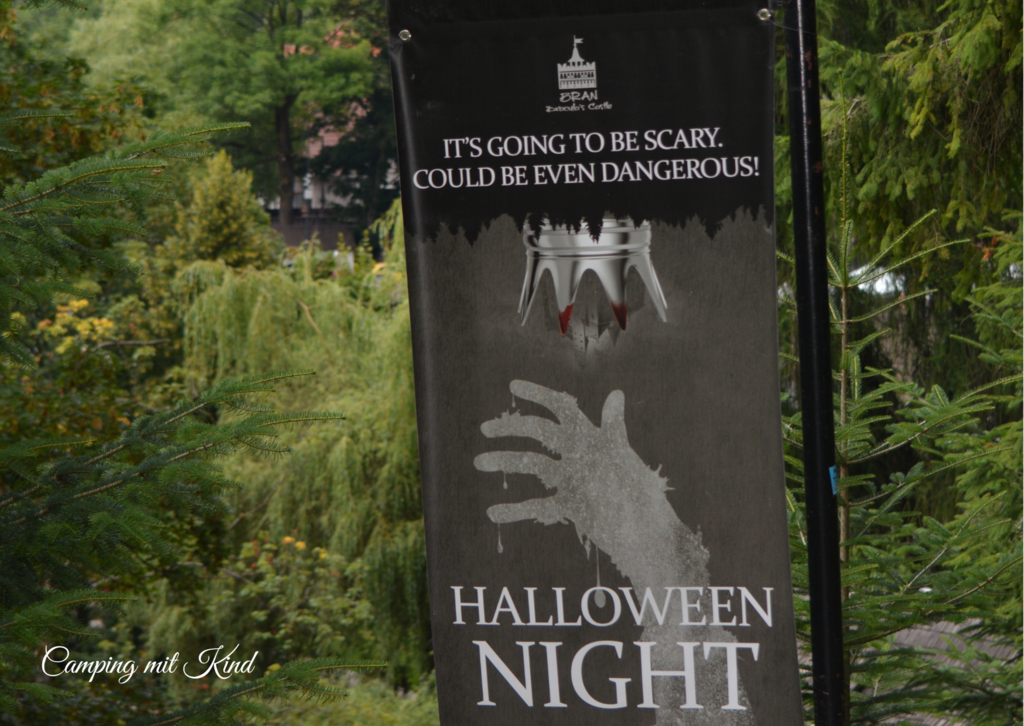 Ein Schild befindet sich auf einer Straßenlaterne. Darauf steht Halloween Night und eine Hand wird gezeigt
