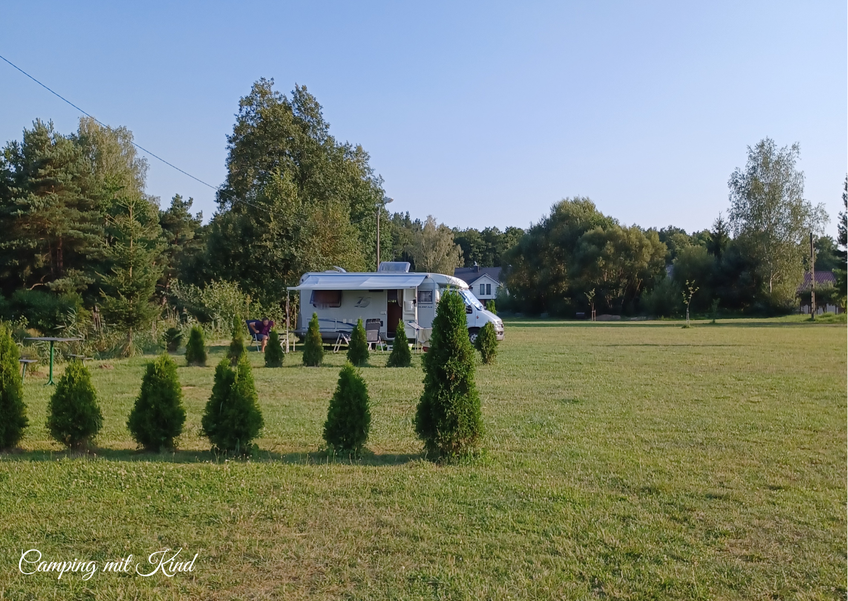 Ein Wohnmobil steht auf einer Wiese. Davor befinden sich Hecken.